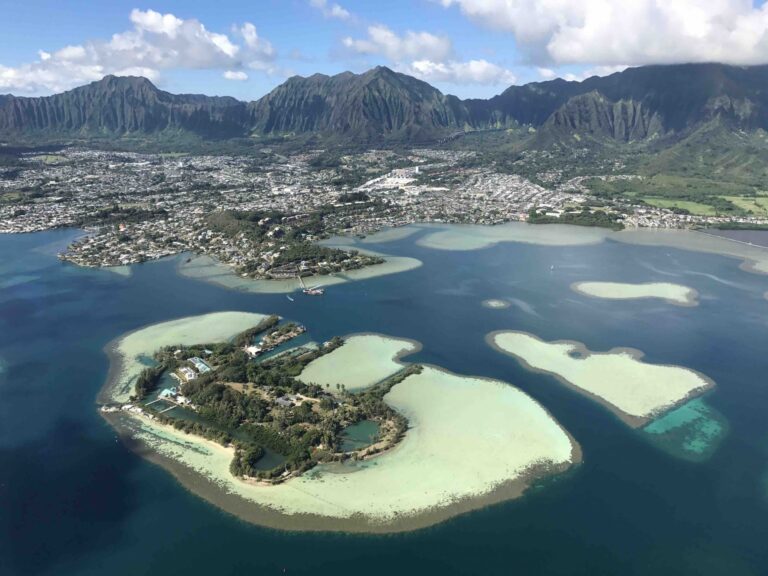 Aerial view of tropical islands, turquoise water, and a coastal town with lush green mountains in the background.