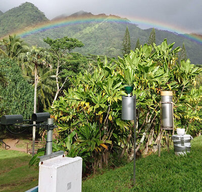 Lush green landscape with weather instruments and a rainbow arching over mountains in the background.