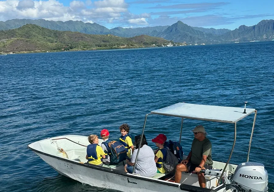 A group of people ride a small motorboat on a lake with mountains in the background under a partly cloudy sky.