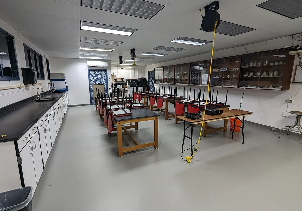 Science classroom with tables, red chairs stacked upside down, cabinets, and lab equipment; room is empty.