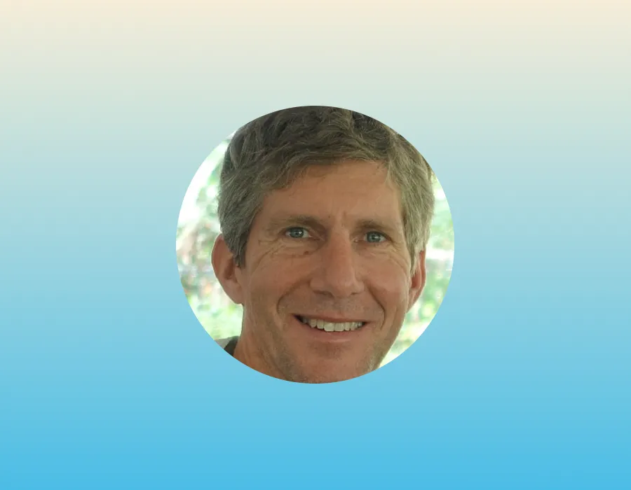 Smiling man with short brown hair, shown in a circular frame on a blue gradient background.