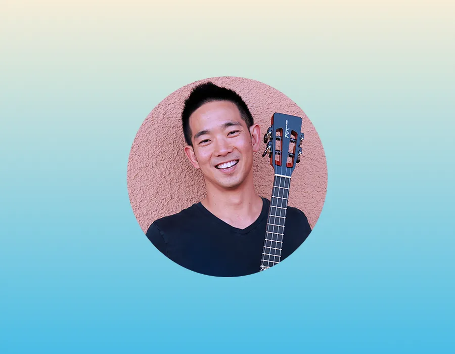 Smiling man holding a ukulele, standing against a peach wall with a blue and beige gradient background.