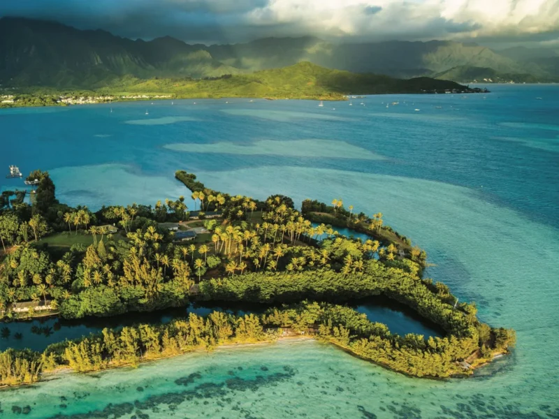 A lush, green tropical island surrounded by turquoise water with mountains in the background.