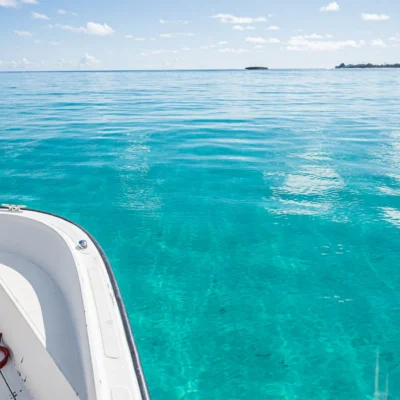 A small white boat floats on clear turquoise water under a bright blue sky with distant land visible.