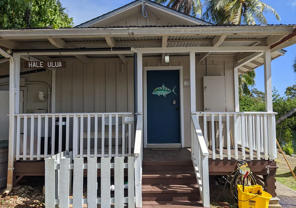 A small building with a fish on the blue door, white railing, and a sign reading "Hale Ulua.