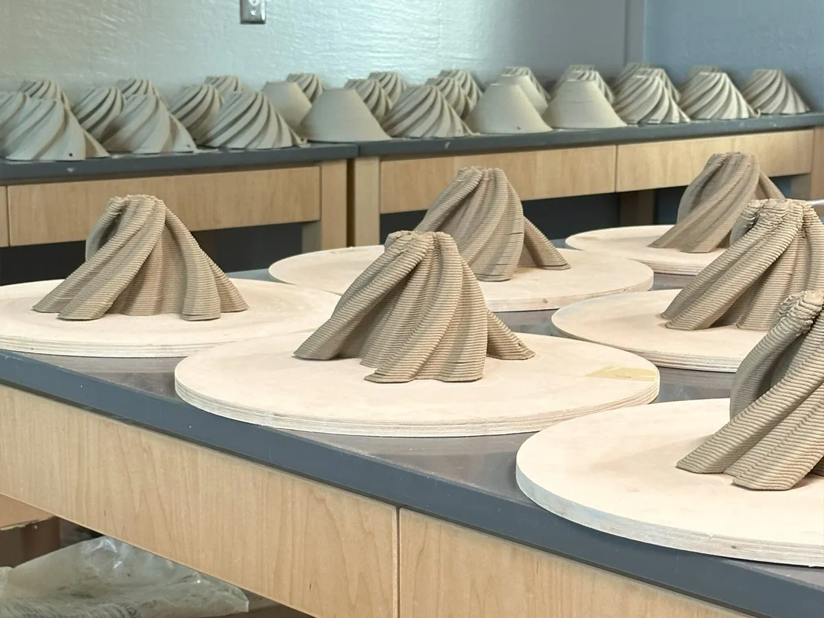 3D-printed clay sculptures in progress on round boards, arranged on wooden tables in a workshop.