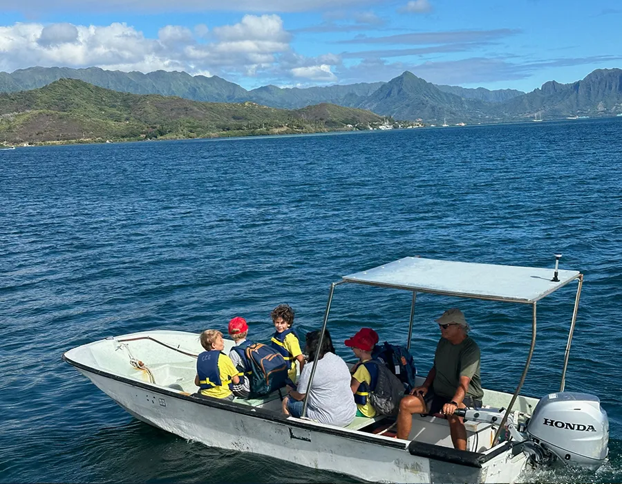 A group of people ride a small motorboat on a lake with mountains in the background under a partly cloudy sky.