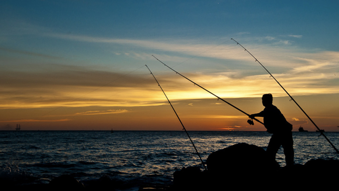 Silhouette of a person fishing by the sea at sunset with fishing rods and colorful sky.