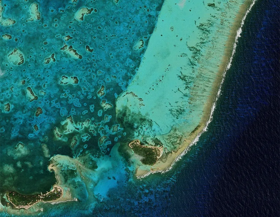 Aerial view of a turquoise coral reef and atoll surrounded by deep blue ocean waters.