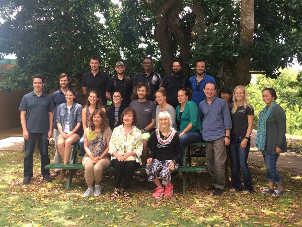 A group of people posing together outdoors on and around benches under trees, smiling at the camera.
